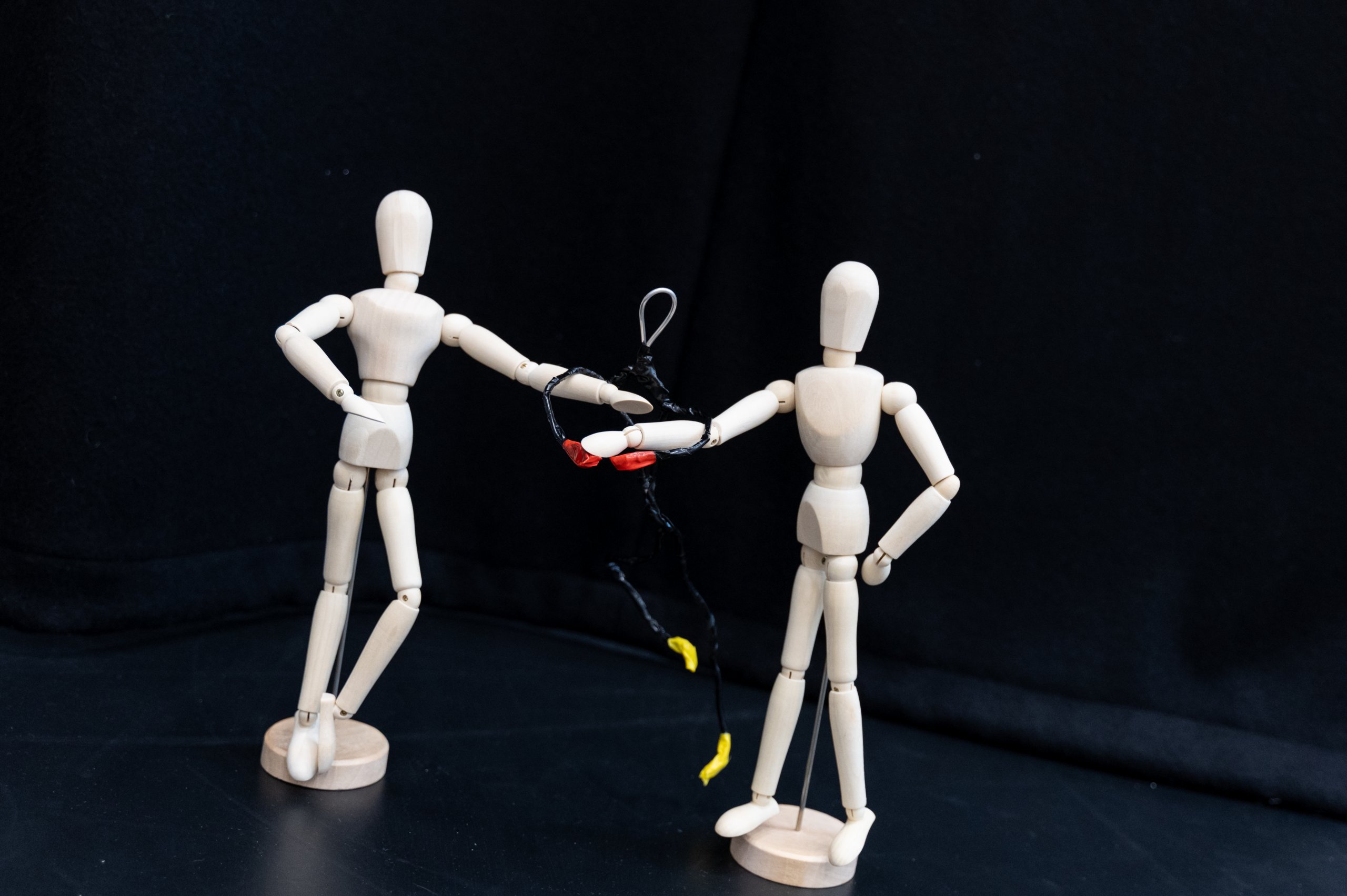 Two small wooden mannequins with a figure made from black wire. 