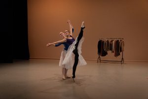 Two ballet dancers in front a rail of clothing